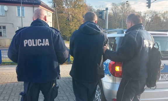 Dwaj policjanci prowadza zatrzymanego mężczyznę do radiowozu.