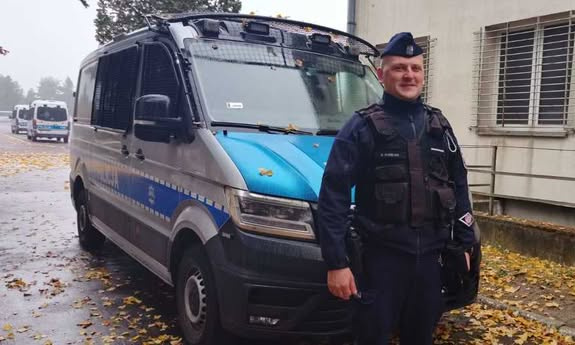 policjant stoi przed radiowozem.