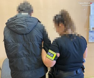 Policjantka z opaską na ramieniu z napisem policja trzyma za ramię zatrzymanego.