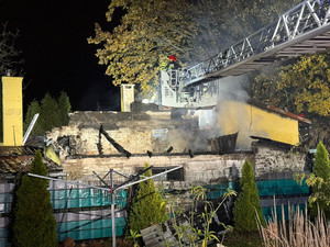 Na zdjęciu widok na spalony budynek mieszkalny. Nad budynkiem, na wysięgniku stoi strażak.