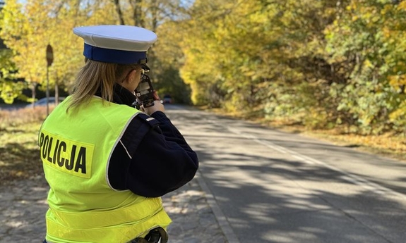 Policjantka stoi przy drodze trzymając fotoradar.