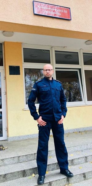 Umundurowany policjant stoi przed budynkiem komisariatu.