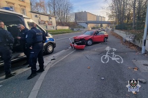 policjanci stoją przy radiowozie, za nimi stoi rozbity samochód.