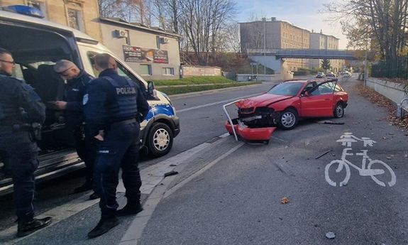 policjanci stoją przy radiowozie, za nimi stoi rozbity samochód.