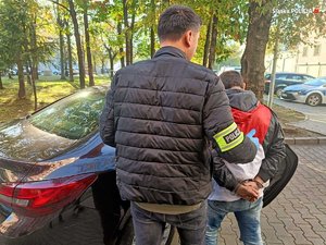 Policjant prowadzi zatrzymana osobę zakutą w kajdanki.