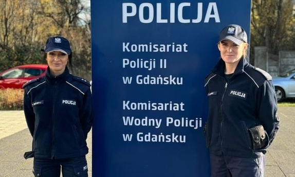 Dwie policjantki stoją przy pylonie informacyjnym przy Komisariacie Policji II w Gdańsku.