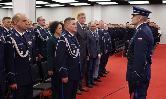 Uczestnicy uroczystości stoją zgromadzeni na sali.