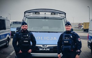 Dwaj policjanci stoją przed radiowozem.