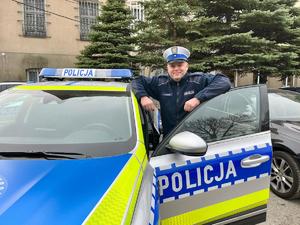 Policjant stoi przy radiowozie.