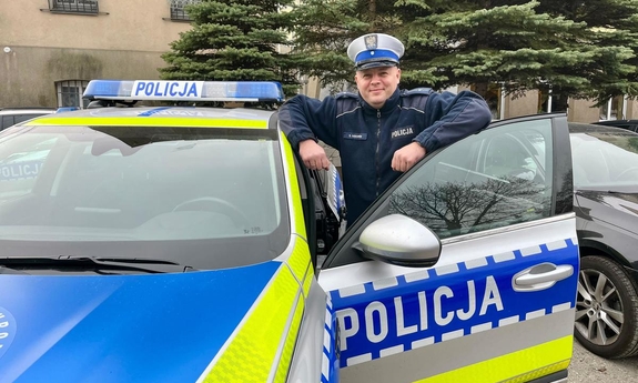 Policjant stoi przy radiowozie.