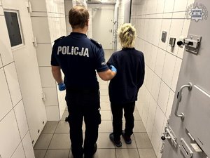 Umundurowany policjant prowadzący korytarzem zatrzymaną kobietę.