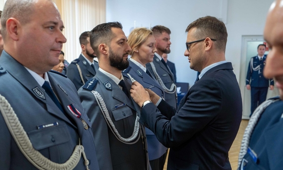 Uczestnicy uroczystości. Policjanci w szeregu. Mężczyzna przypina medal jednemu z nich.