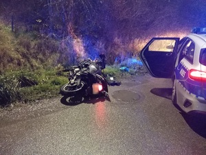 Motocykl leżący przy jezdni obok zaparkowany radiowóz z włączonymi sygnałami.