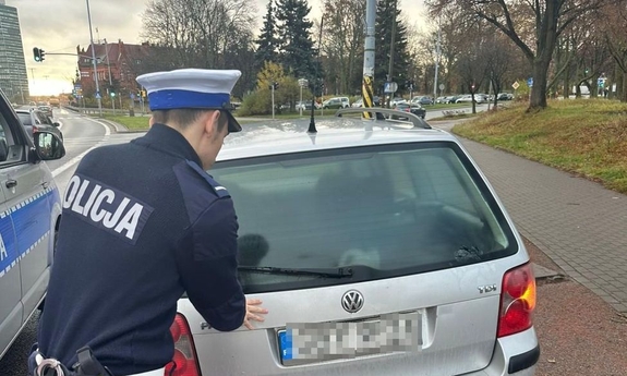 Policjant przy zepsutym samochodzie w kolorze szarym.