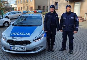 Policjant i policjantka stoją przy radiowozie.