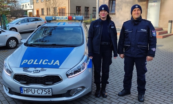 Policjant i policjantka stoją przy radiowozie.