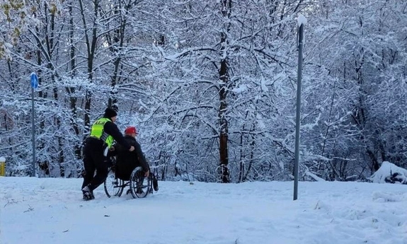 Na zdjęciu policjant pomaga niepełnosprawnemu mężczyźnie na wózku inwalidzkim.