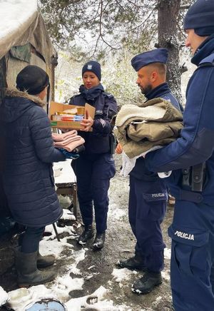 Trzej policjanci stoją z darami w rękach, obok nich kobieta.