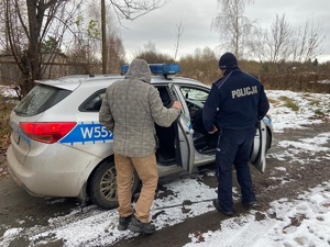 Na zdjęciu umundurowany policjant i mężczyzna wsiadają do radiowozu.