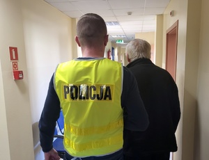 Policjant prowadzi zatrzymanego mężczyznę.