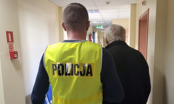 Policjant prowadzi zatrzymanego mężczyznę.