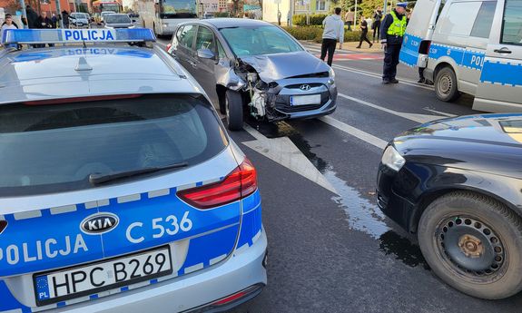 obok radiowozu stoi uszkodzony samochód.