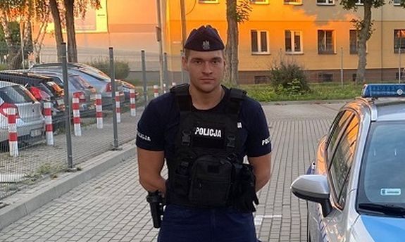 policjant stoi obok radiowozu.