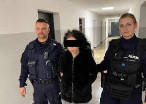 Policjant i policjantka prowadzą zatrzymaną osobę korytarzem.