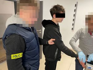 Policjant i policjantka prowadzą zatrzymaną osobę korytarzem.