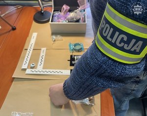 Na zdjęciu opaska policja na ramieniu oraz biżuteria trzymana przez policjanta.