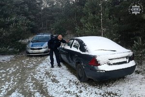 Zdjęcie przedstawia radiowóz oraz policjanta zerkającego przez szybę do pojazdu osobowego.