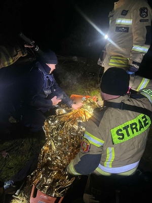 Policjanci i strażacy z OSP udzielają pomocy odnalezionej kobiecie.