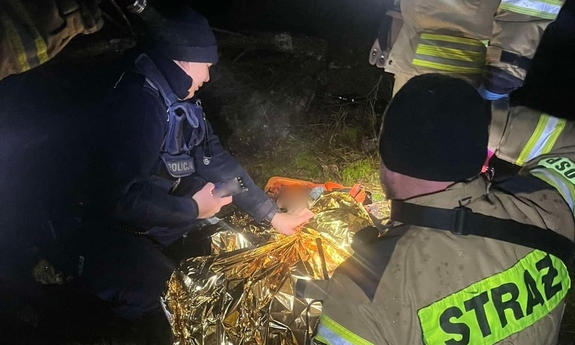 Policjanci i strażacy z OSP udzielają pomocy odnalezionej kobiecie.