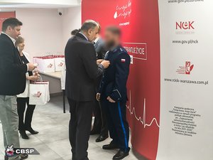 Na zdjęciu mężczyzna wręcza odznaczenie umundurowanemu policjantowi.