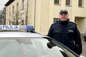 policjant stoi obok radiowozu.