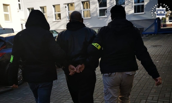 Dwaj funkcjonariusze prowadzą zatrzymanego.