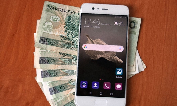 Smartfon lezy na rozłożonych banknotach 100-złotowych.