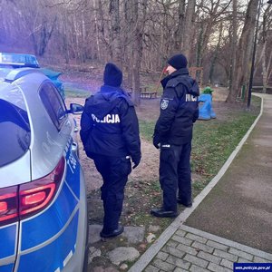 Na zdjęciu umundurowani policjanci stoją obok radiowozu.