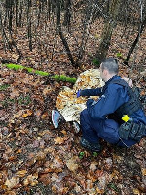 las, na ziemi leży mężczyzna okryty przez policjanta kocem.