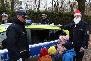 Czworo dzieci przy radiowozie policyjnym razem z policjantami - jeden z nich ma na głowie czapkę Mikołaja.