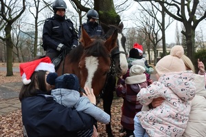 Dwoje policjantów na koniach, obok grupa dzieci z policjantami.