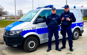 Dwóch umundurowanych policjantów stoi przy radiowozie.