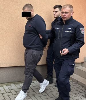 Dwaj umundurowani policjanci prowadzą zatrzymanego.