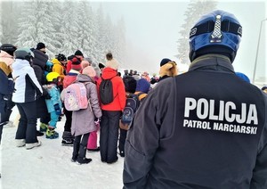 Policjant z patrolu narciarskiego obserwuje osoby na stoku.