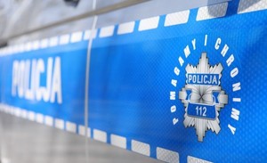 Napis Policja i logo Pomagamy i chronimy na drzwiach radiowozu policyjnego.