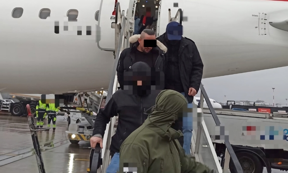 Policjanci wyprowadzają zatrzymanego z samolotu.