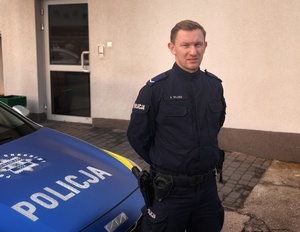 policjant stoi przy radiowozie.