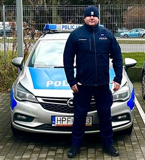 Policjant stoi przed radiowozem policyjnym.