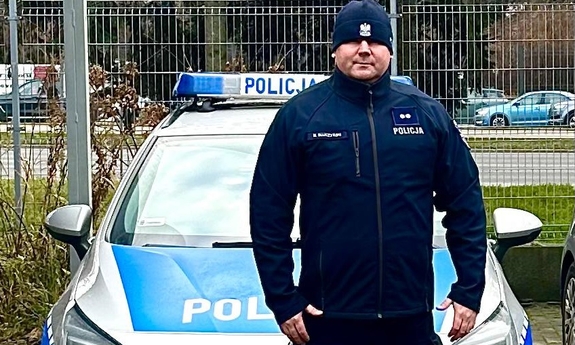 Policjant stoi przed radiowozem policyjnym.