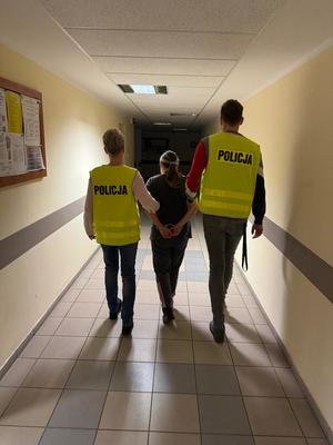 Policjanci prowadzą zatrzymaną kobietę.